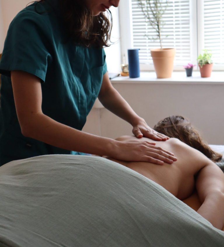Femme recevant un massage sur une table, avec une praticienne à proximité.